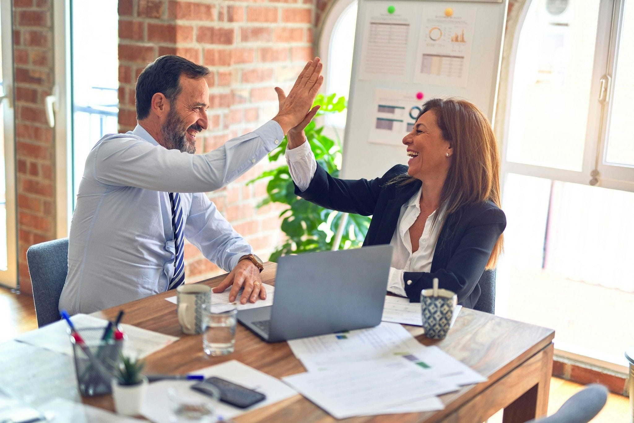 Two colleagues high-fiving across a desk with a laptop
