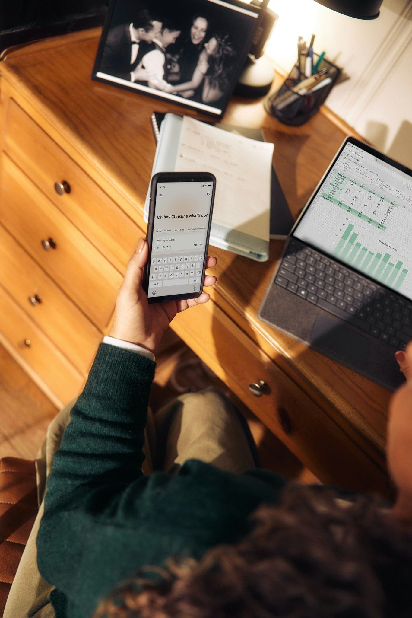 Person holding a phone above a desk with a laptop and a tablet
